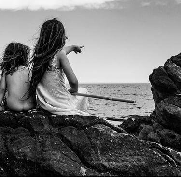 two girls sitting on rocks with a stick in their hands
