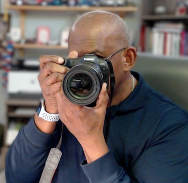 A male photographer holding a professional Canon EOS DSLR camera to his eye to take a picture.