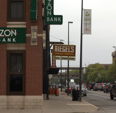 Exterior of Horizon Bank and Riegel's Pipe and Tobacco shop on a busy city street with traffic.