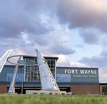Fort Wayne International Airport terminal building exterior featuring a modern metal sculpture under a cloudy sky.