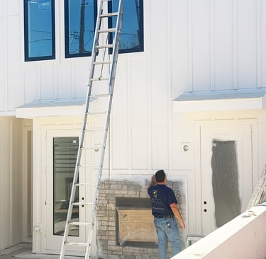 Professional painter prepping a white board and batten home exterior for modern house siding repair.