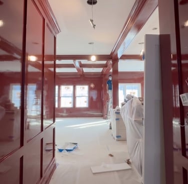 Professional painter applying high-gloss red lacquer finish to custom home library wood paneling.