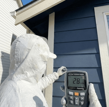 a person in a white painter suit measuring paint thickness - daeco paintng