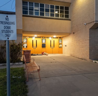 Homeless person sleeping by doors of a school next to a no trespassing sign