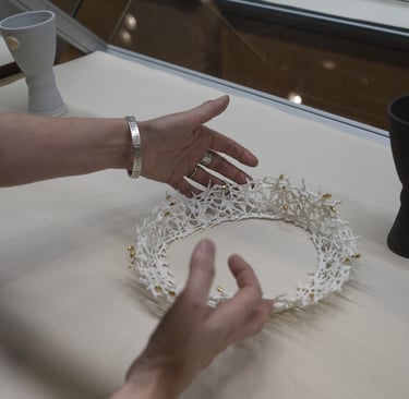 Two hands carefully place a white porcelain crown sculpture with gold details in a display case