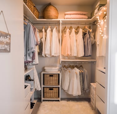 Organized walk-in closet with hanging white shirts, wicker baskets, and a plush rug.