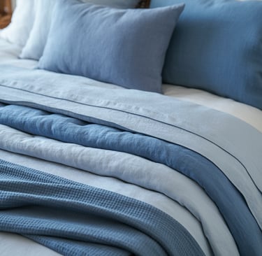 Layered blue linen bedding and textured waffle throw blanket on a cozy made bed.