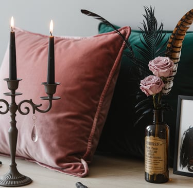 Gothic home decor featuring a black candelabra with lit candles, velvet pillows, and dried roses in a vintage bottle.