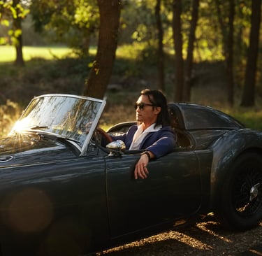 A photo of a man sitting in a 1958 MG MGA Roadster at sunset