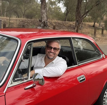 Image of a man sitting in a red 1974 Alfa Romeo smiling at the camera