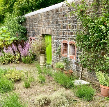 Rustic stone garden wall with a bright green wooden door, potted plants, and blooming lavender.