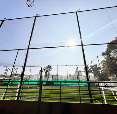 Wide shot of a sports practice net enclosing a cricket pitch under bright sunlight.
