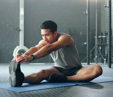 a man is stretching his legs on a mat with a bottle of water