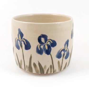 Handmade ceramic cup featuring hand-painted blue iris flowers on a cream glaze.