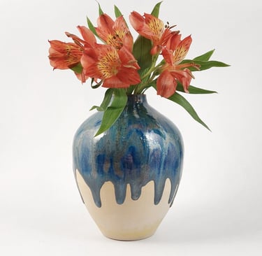 Handmade ceramic vase with blue drip glaze holding a bouquet of orange Alstroemeria flowers.