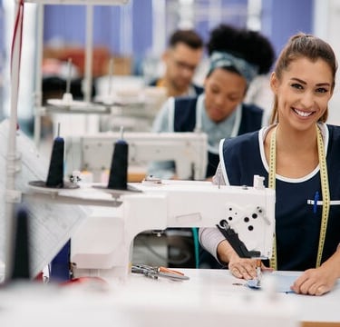 Smiling female seamstress working at an industrial sewing machine in a garment factory.