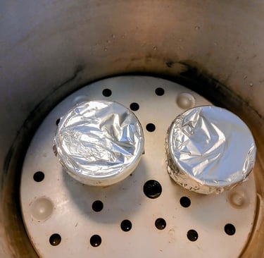two jars with foil on lids sitting in a pressure cooker