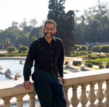 Foto do Mestre Mauricio apoiado em uma mureta, com um lago e um jardim ao fundo.