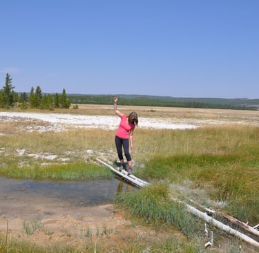 a woman standing on a log bridge over fairy creek, Yellowstone national park