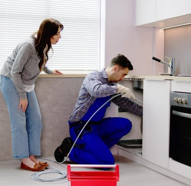 A plumber and woman home owner, working on a kitchen drain blockage.
