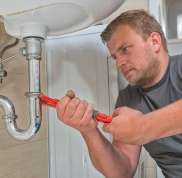 a plumber in a gray shirt is holding a wrench