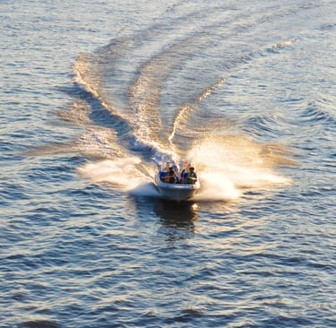 A motorboat speeds across blue water at sunset, leaving a white wake in its trail.