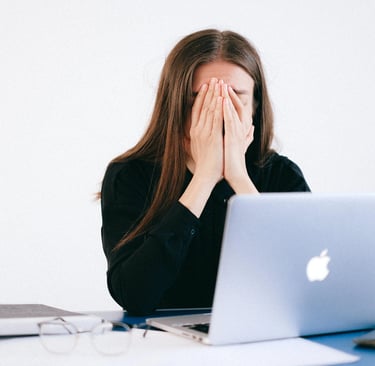 Une femme assise à son bureau se cache le visage avec ses mains devant son ordinateur