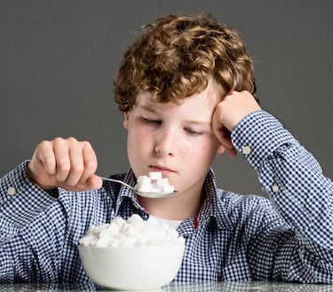 a boy eating cubes of sugar in spoon from glass bowl