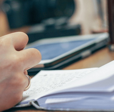 Person writing in a journal, with a cup placed nearby