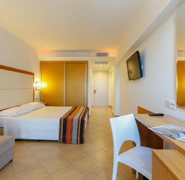 Modern hotel room with queen bed, seating area, desk, and flat-screen TV.