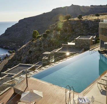Luxury infinity pool at a cliffside Mediterranean resort overlooking the blue sea and rugged mountains.