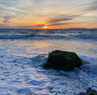 Golden sunset over ocean waves with a moss-covered rock in the white sea foam.