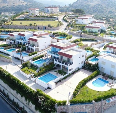 Aerial view of luxury vacation villas with private swimming pools in a hillside Greek resort.
