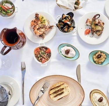 An overhead view of a Mediterranean seafood spread with grilled octopus, mussels, and shrimp on a white tablecloth.