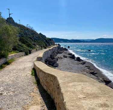A scenic coastal walking path along a rocky beach with blue ocean water under a clear sky.