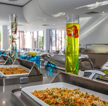 Gourmet hotel buffet with hot pasta dishes in silver chafing servers and tall decorative vases.