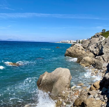 blue sea, some rocks and rhodes city on background