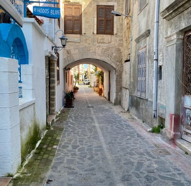 A narrow cobblestone street in Rhodes Old Town featuring a stone archway and Mediterranean architecture.