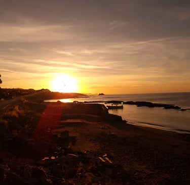 Golden sunset over a rocky coastline with a calm ocean beach and a small boat at dusk.
