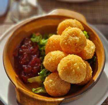 Golden fried cheese balls appetizer served with cranberry sauce and fresh greens in a ceramic bowl.
