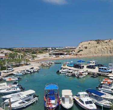 Aerial view of small boats docked in a turquoise harbor by a sandy beach with limestone cliffs.