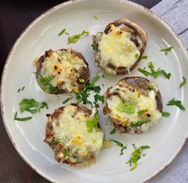 Four baked mushrooms stuffed with melted cheese and fresh herbs on a white ceramic plate.
