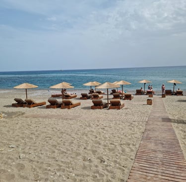 Luxury beach resort with straw umbrellas and wooden lounge chairs on a sandy shore by the blue ocean.