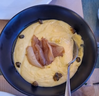 Greek fava dip in a black bowl topped with caramelized onions and capers.
