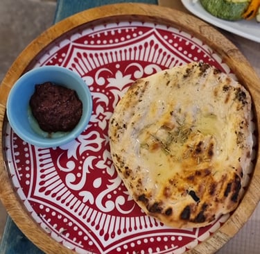Freshly baked pita bread with olive oil and rosemary served with olive tapenade on a decorative red plate.