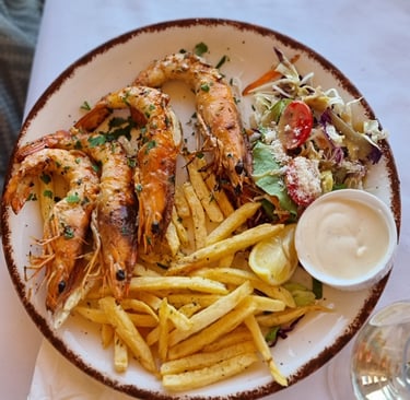 Grilled prawns served with crispy french fries, fresh garden salad, and creamy dipping sauce on a white plate.