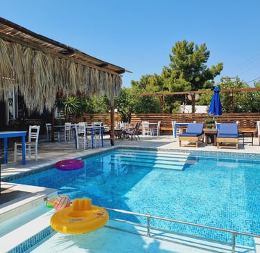 Luxury outdoor resort swimming pool with lounge chairs, dining tables, and a tropical thatched roof.