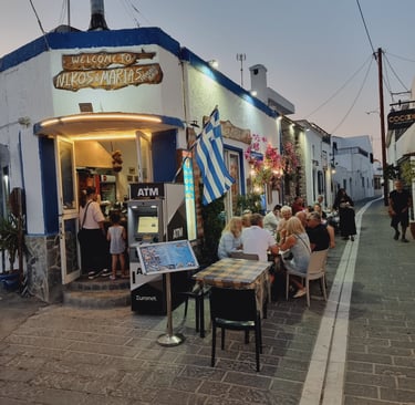 Customers dining outdoors at Nikos and Marias Greek restaurant on a cobblestone street in Naxos.