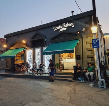 Customers sitting outside South Bakery at dusk with green awnings and glowing shop lights.