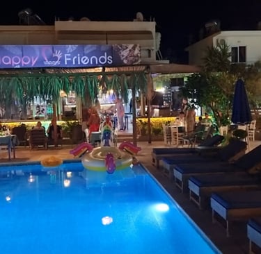 Night view of Happy Friends poolside bar with lit swimming pool and outdoor seating area.